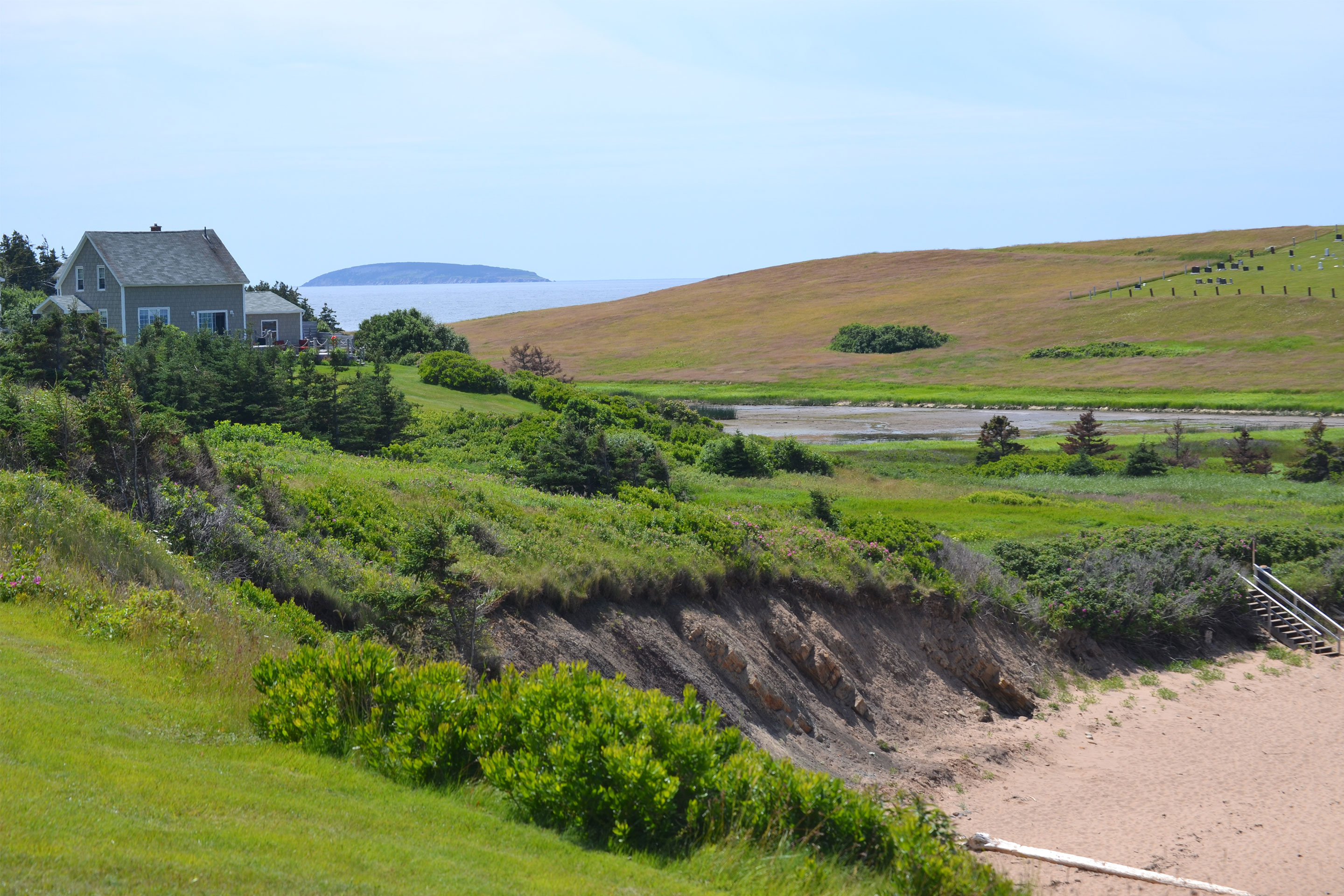 An image showing the ocean in the distance and greenery with a house perched on a hill in the middle ground. 